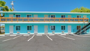 A two-story motel with a blue exterior, a balcony with a wooden railing, and a parking lot in front.