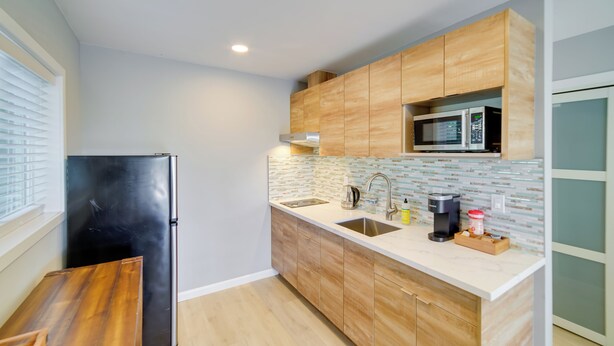 A modern kitchen with wooden cabinets, a stainless steel refrigerator, a microwave, and a sink.