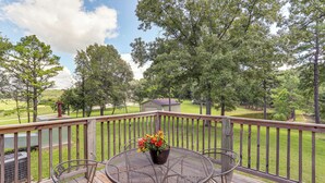 A wooden deck with a metal table and chairs, a potted plant, and a view of a green landscape with trees and a building in the distance. - Rural Melbourne House With Deck! (Melbourne)