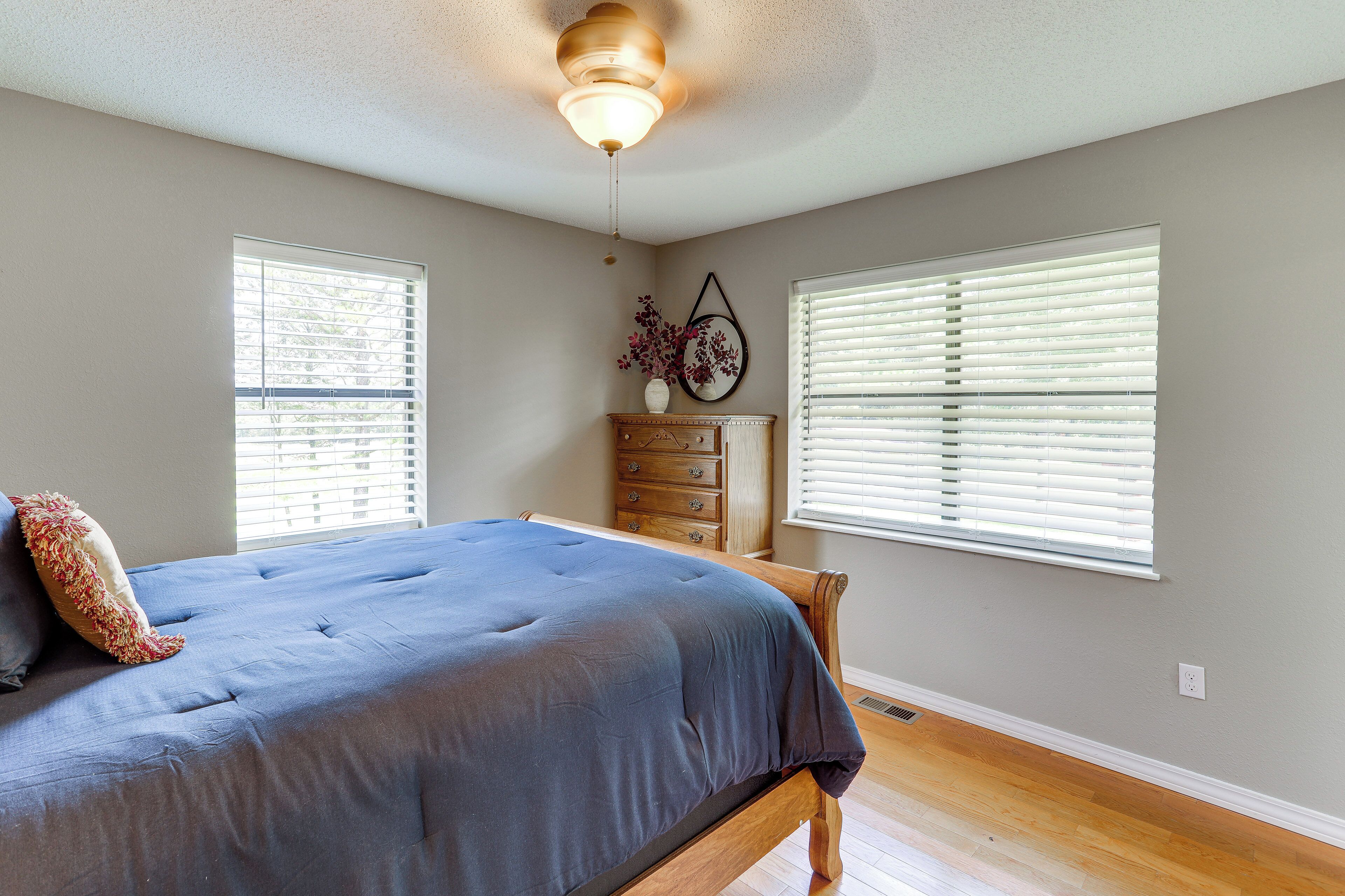 Un dormitorio con cama, cómoda y dos ventanas con persianas.