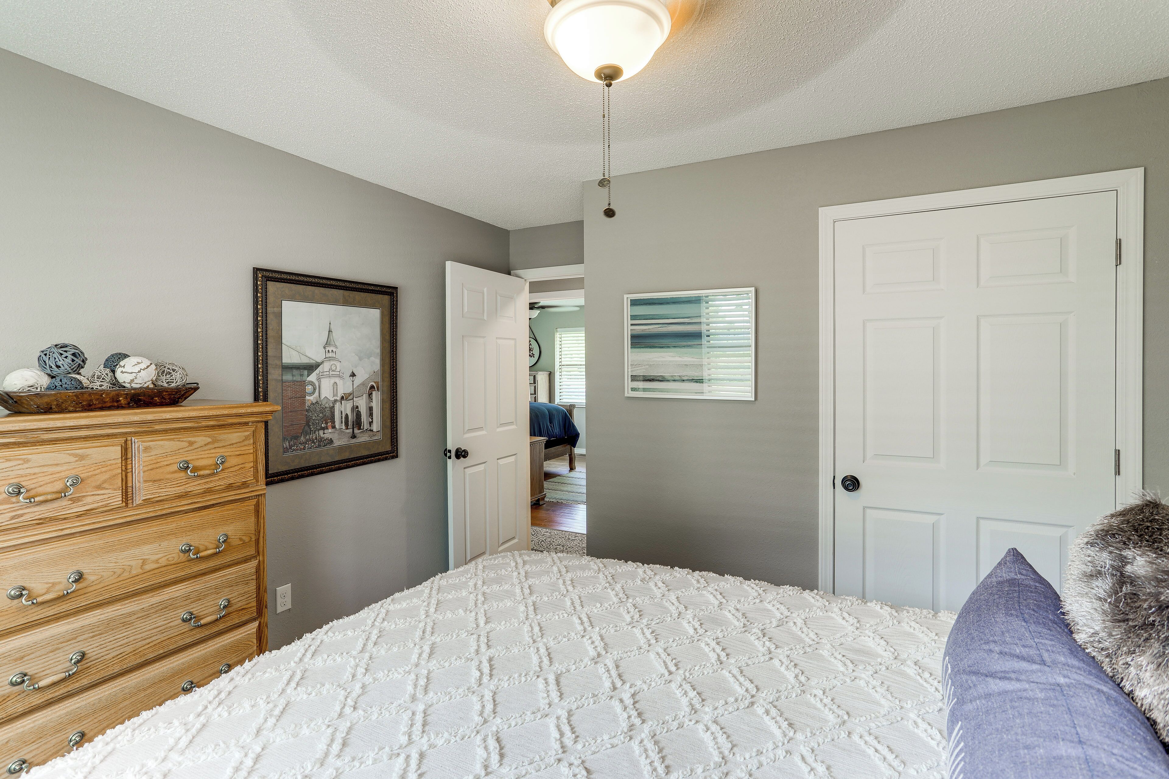 A bedroom with a bed, dresser, and a door leading to another room.