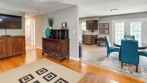 A spacious living room with hardwood floors, a large TV, and a dining area with blue chairs and a table. - Rural Melbourne House With Deck! (Melbourne)
