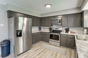 A modern kitchen with stainless steel appliances, dark cabinetry, and a marble countertop.