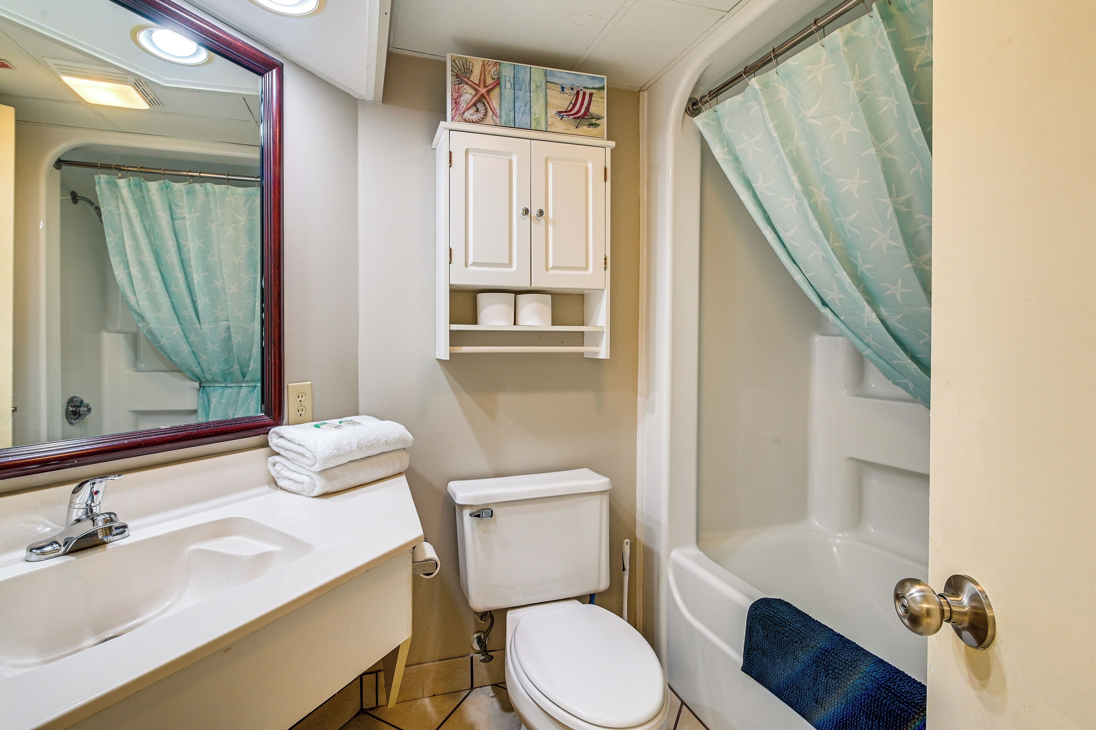 Een badkamer met een witte wasbak, toilet en bad. Boven de wasbak hangt een spiegel en er is een handdoekrek met handdoeken.