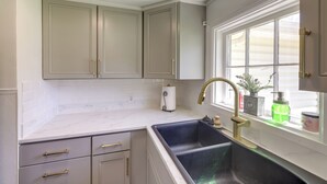 A kitchen with a double sink, white cabinets, and a window with plants.