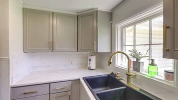 A kitchen with a double sink, white cabinets, and a window with plants.