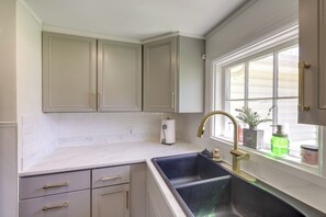 Een keuken met een dubbele spoelbak, witte kastjes en een raam met planten.