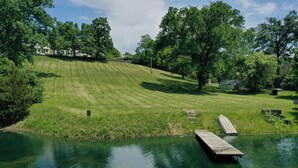A serene lakeside setting with a wooden dock extending into the water, surrounded by lush greenery and trees.