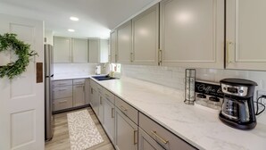 A modern kitchen with white cabinets, a stainless steel refrigerator, a coffee maker, and a decorative plant.