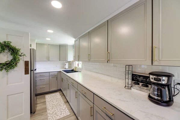 A modern kitchen with white cabinets, a stainless steel refrigerator, a coffee maker, and a decorative plant.