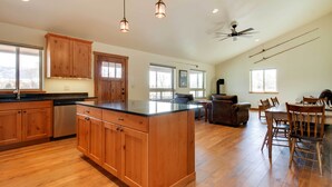 A spacious kitchen with wooden cabinets, a large island, and a dining area with a table and chairs. - Beautiful Jefferson River Cabin w/ Mountain Views! (Twin Bridges)