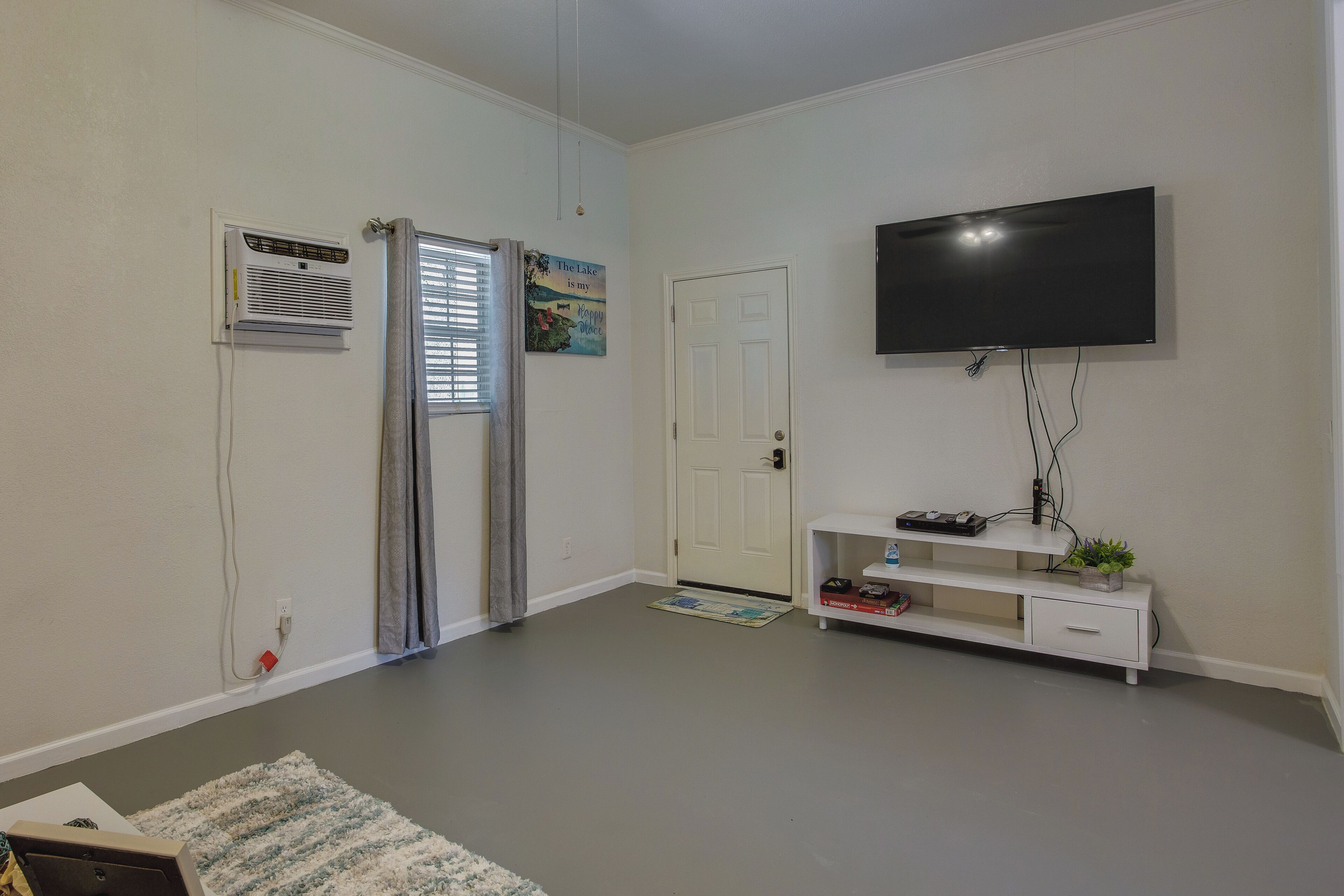 A living room with a flat-screen TV mounted on the wall, a white entertainment unit with a plant, and a door with a window.