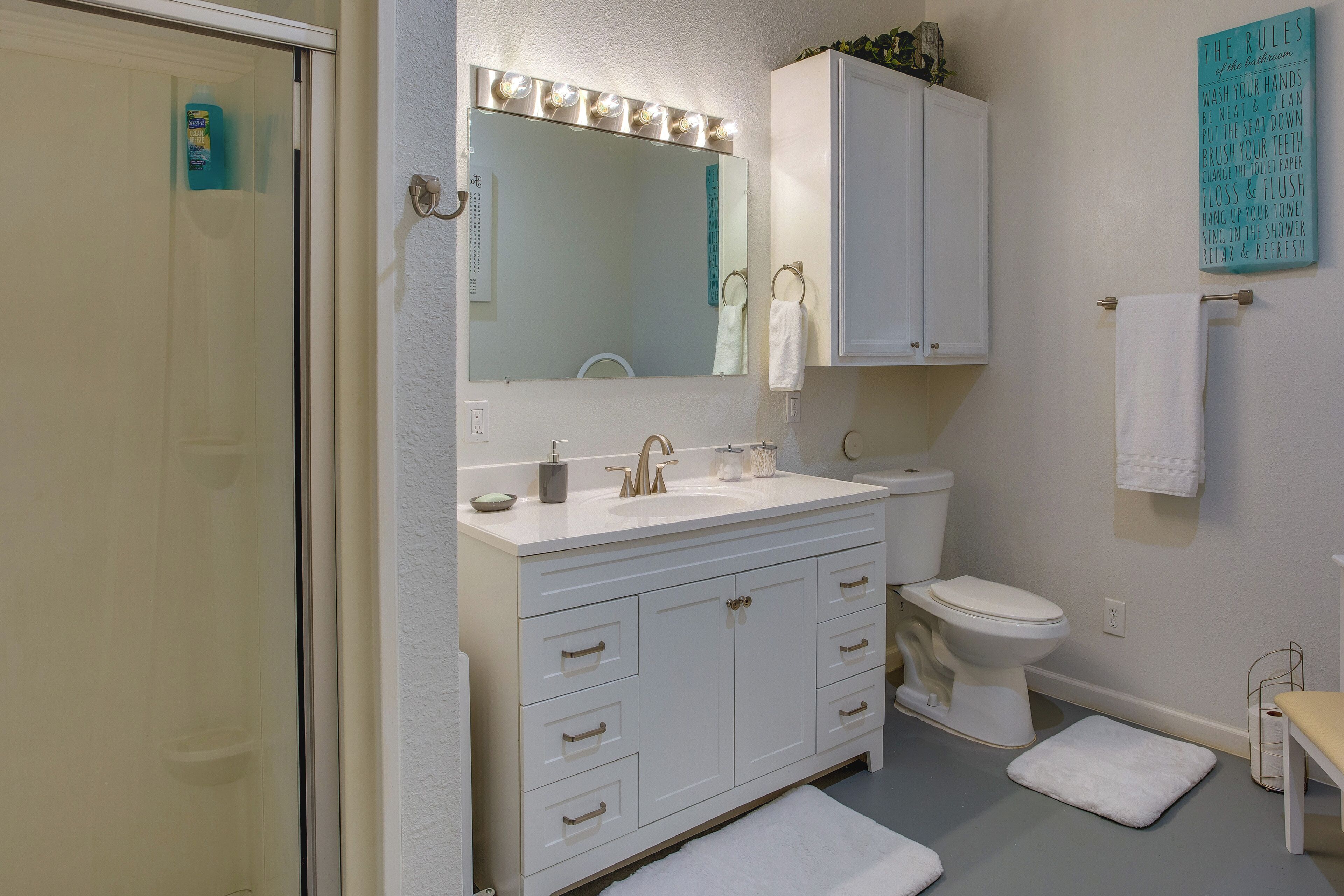 A bathroom with a white vanity, a mirror with lights, a toilet, and a towel rack.