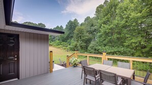 A deck with a table and chairs, a door, and a view of a wooded area.