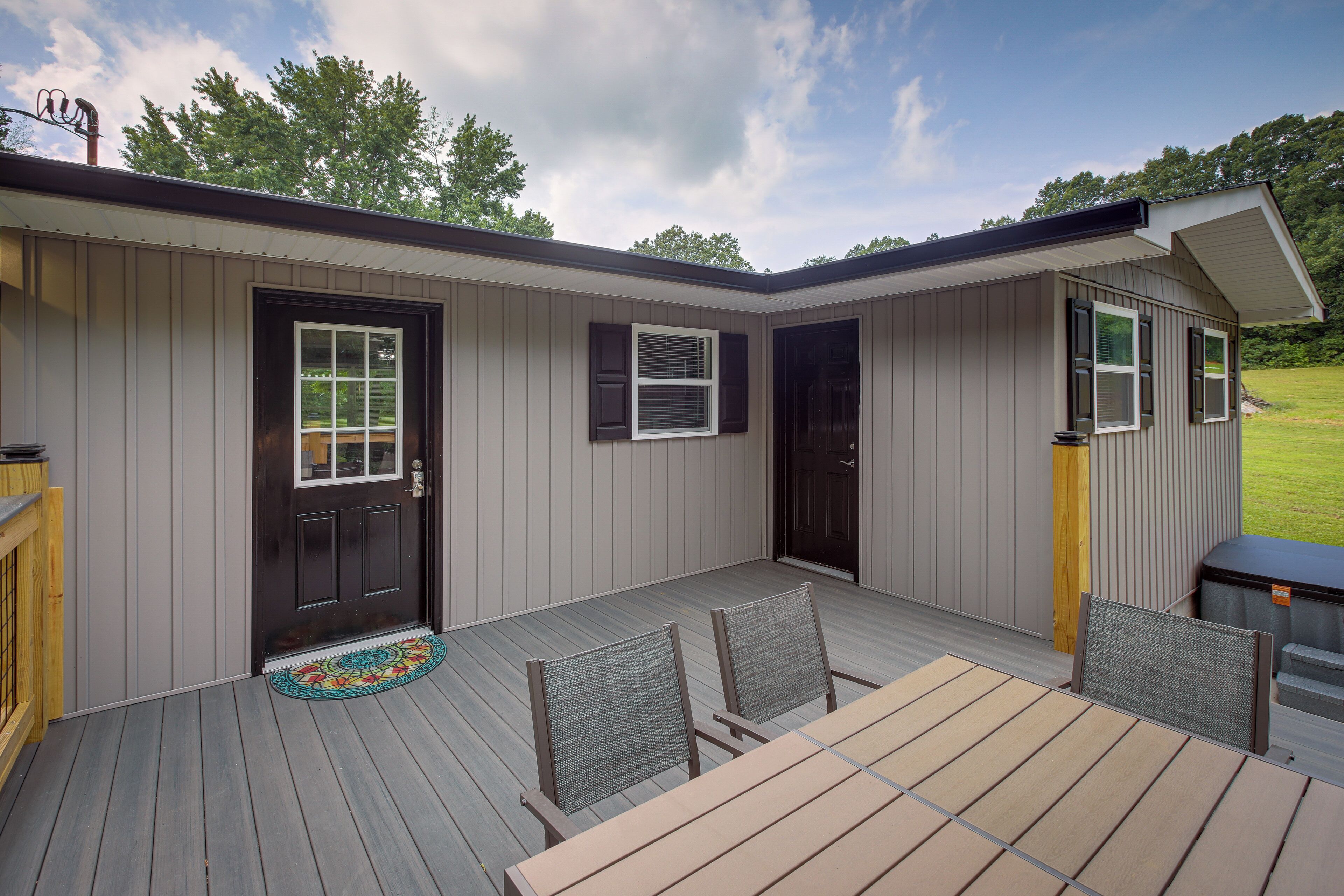 A covered deck with a table and chairs, a door, and a small outdoor seating area.