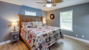 A bedroom with a wooden bed, a nightstand with a lamp, a ceiling fan, and a window with blinds.