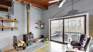 A spacious living room with a fireplace, wooden floors, and a large sliding glass door leading to an outdoor deck. - 'alpine House' Modern Delevan Cabin on 2 Acres (Delevan)