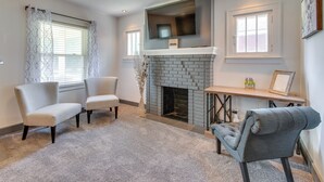 A living room with a fireplace, two armchairs, a sofa, and a TV mounted above the fireplace.