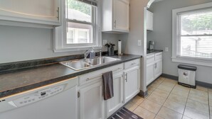 A kitchen with white cabinets, a black countertop, a dishwasher, and a window with blinds.