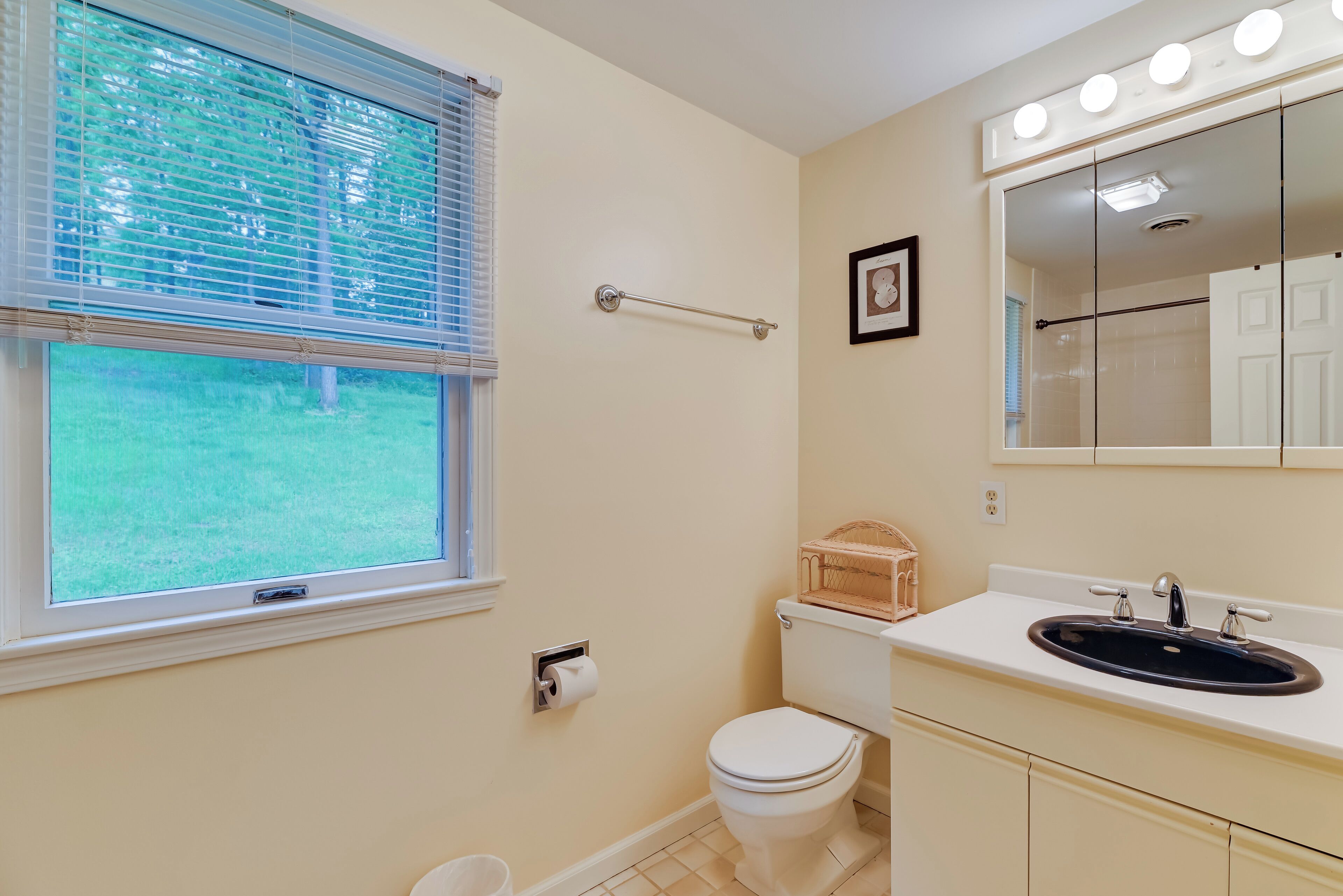 A bathroom with a toilet, sink, and window with blinds.