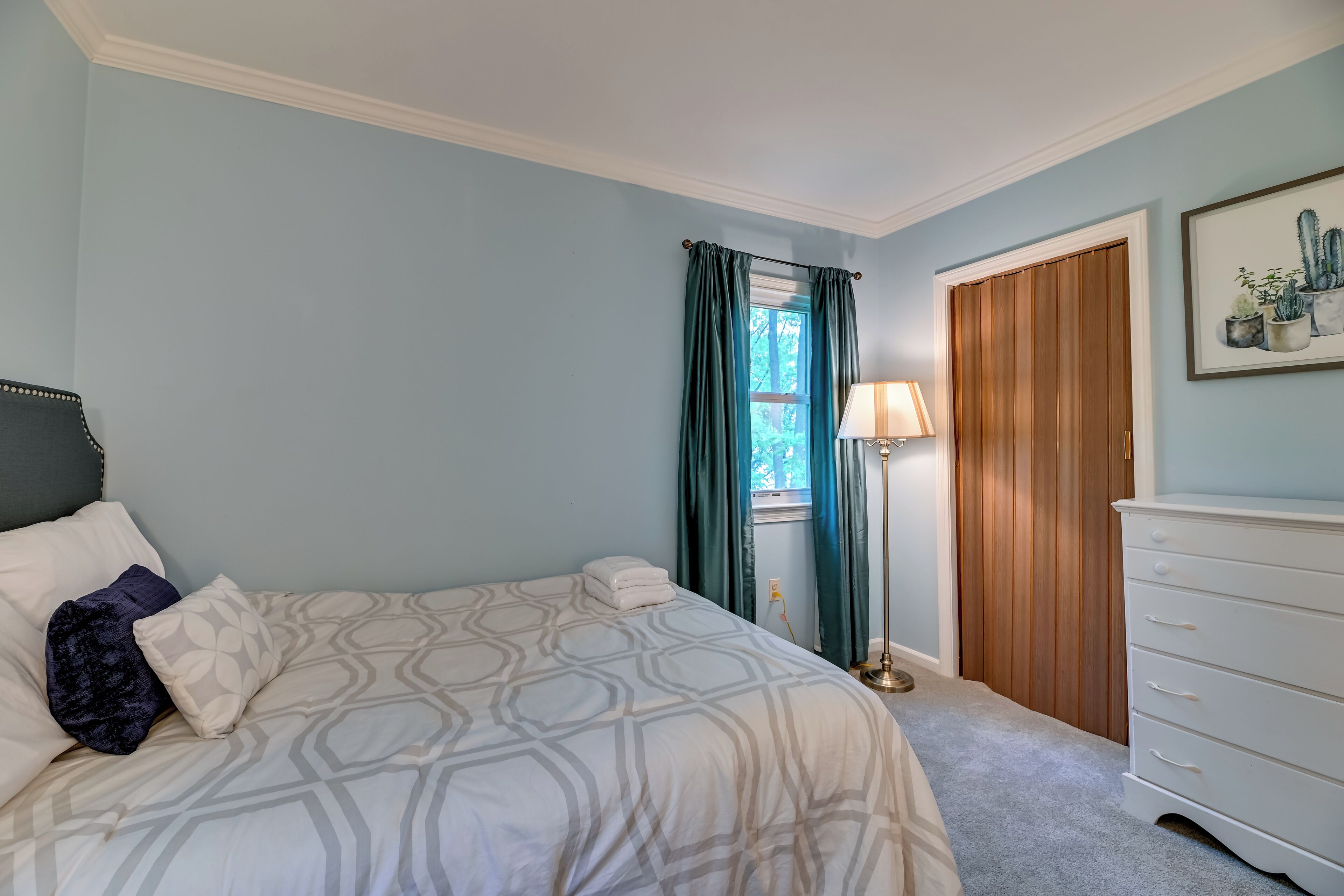 A bedroom with a bed, a dresser, a lamp, and a window with curtains.