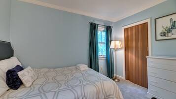 A bedroom with a bed, a dresser, a lamp, and a window with curtains.