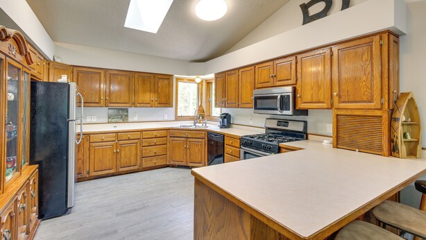 A kitchen with wooden cabinets, a refrigerator, a stove, a microwave, and a large island. - Faribault Home w/ Deck Near Cedar Lake Boat Ramp! (Faribault)