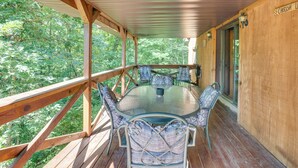 A covered outdoor deck with a glass-top table and chairs, surrounded by wooden railings and a view of the forest. - French Lick Getaway w/ Deck, Grill & Fire Pit! (French Lick)
