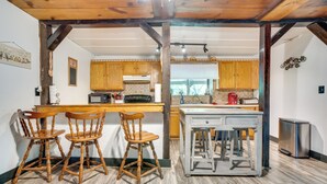 A kitchen with wooden cabinets, a central island with stools, a microwave, and a coffee maker. - French Lick Getaway w/ Deck, Grill & Fire Pit! (French Lick)
