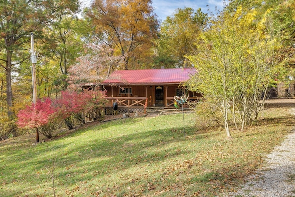 A rustic cabin with a red roof, surrounded by autumn foliage.