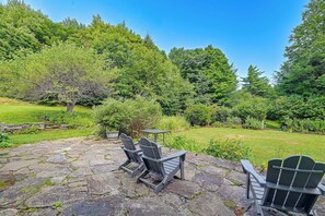 A stone patio with Adirondack chairs and a table, surrounded by lush greenery and trees. - Marlboro Escape: 9 Mi to Mount Snow Resort! (Wilmington)