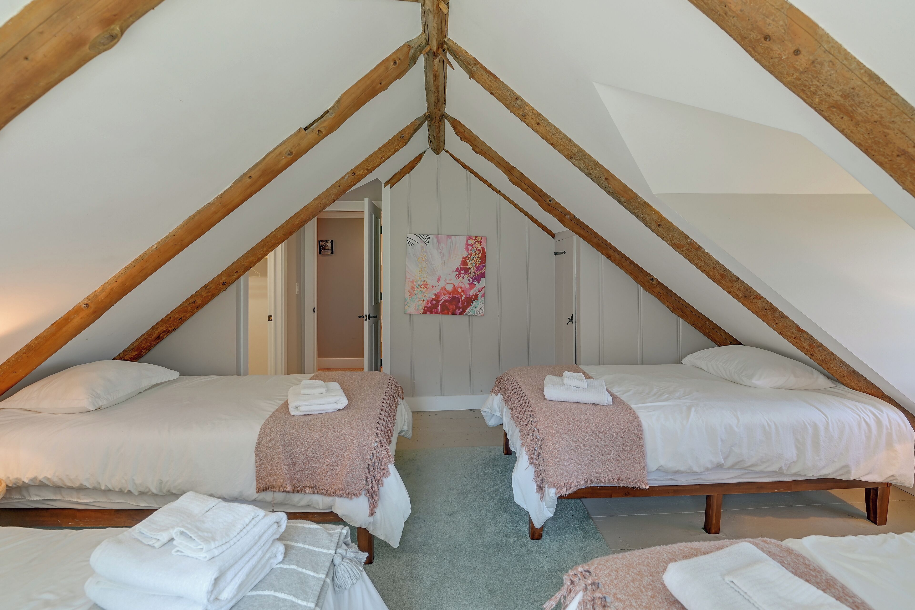 A bedroom with two beds, a wooden ceiling, and a door leading to another room.