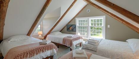 A cozy attic bedroom with two beds, a television, and a window with a view of greenery.