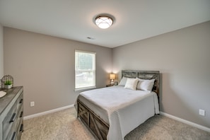 A bedroom with a bed, nightstand, dresser, and a window with blinds.