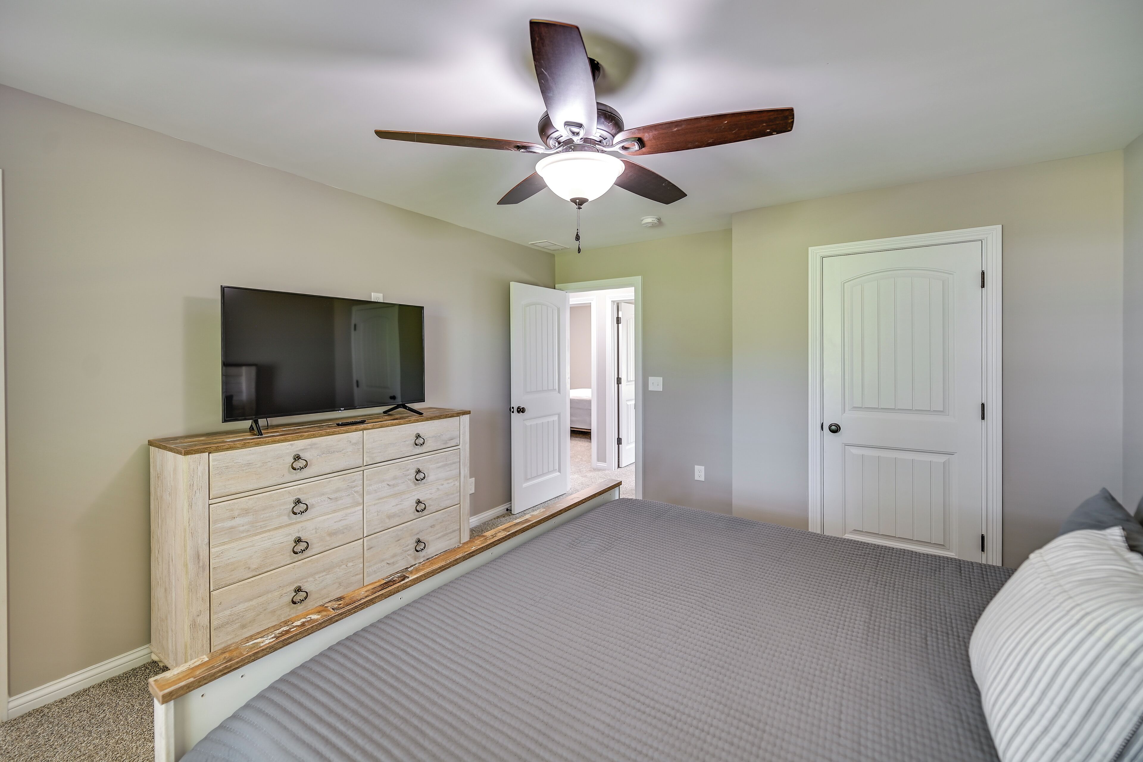 A bedroom with a bed, a dresser, a television, and a ceiling fan.