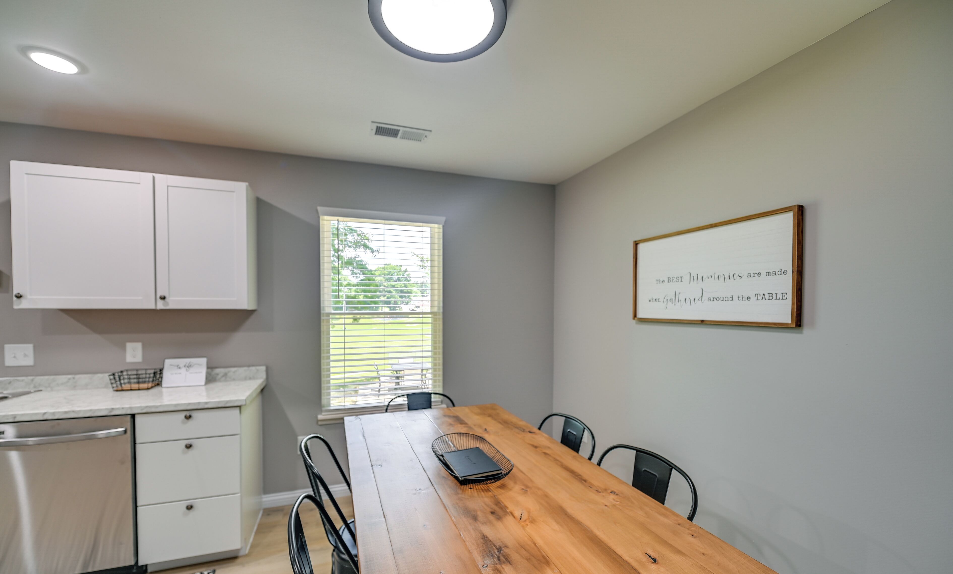 A dining area with a wooden table, chairs, a white cabinet, and a framed quote on the wall.