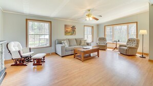 A spacious living room with hardwood flooring, a ceiling fan, a fireplace, and large windows. - Near Waterville: Cozy Midcoast Vacation Rental! (Albion)