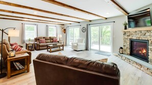 Un salon spacieux doté d’une cheminée, de poutres apparentes, de sièges confortables et de grandes fenêtres.