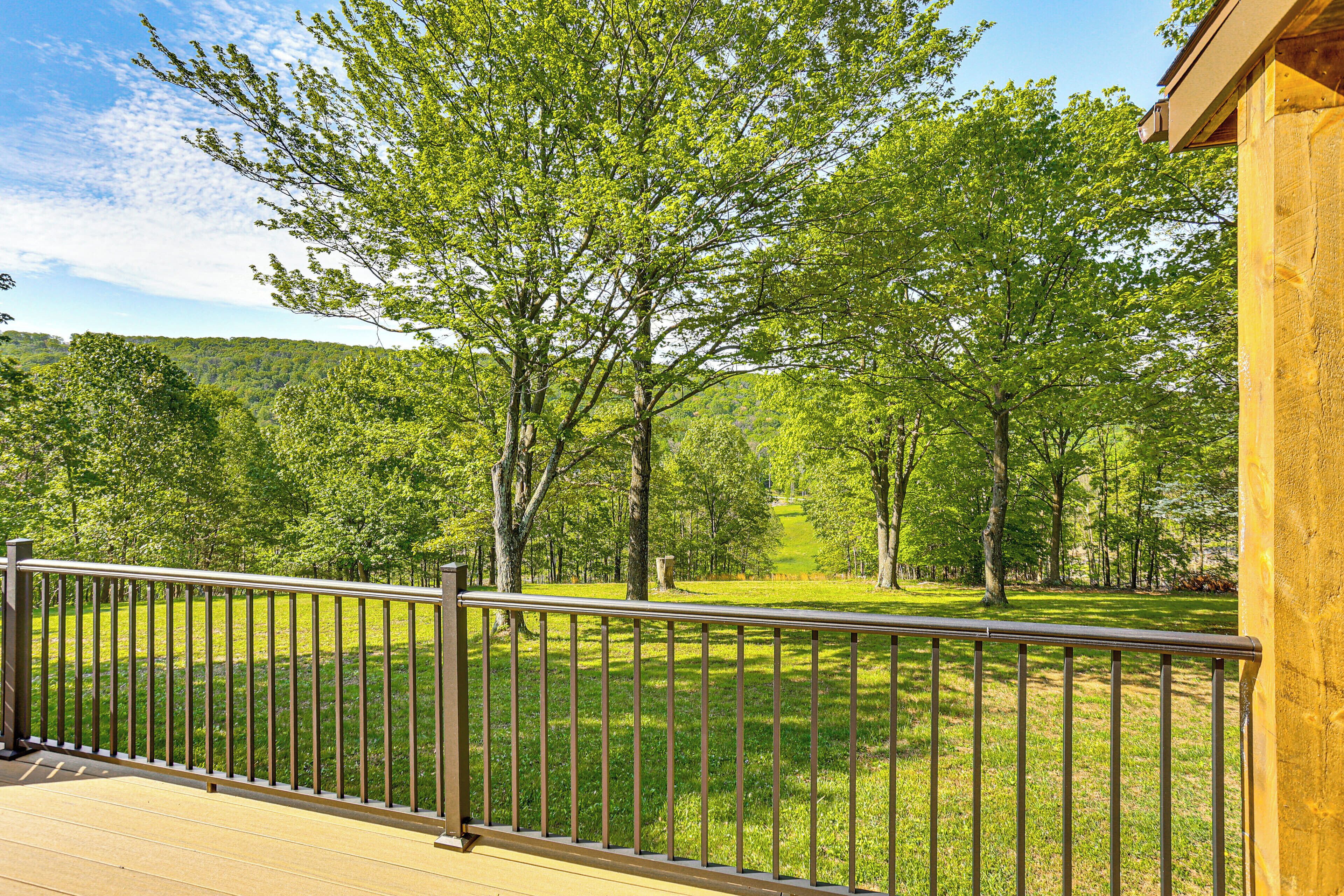 A wooden deck with a metal railing overlooking a grassy area with trees.