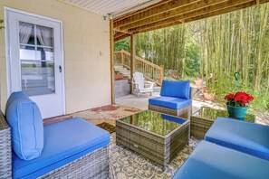 A covered patio area with wicker furniture, a white chair, and a staircase leading to a garden.