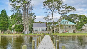 A wooden dock leading to a house with a blue roof, surrounded by trees and a calm body of water. - Waterfront Vacation Property on the Pamlico (Bath)