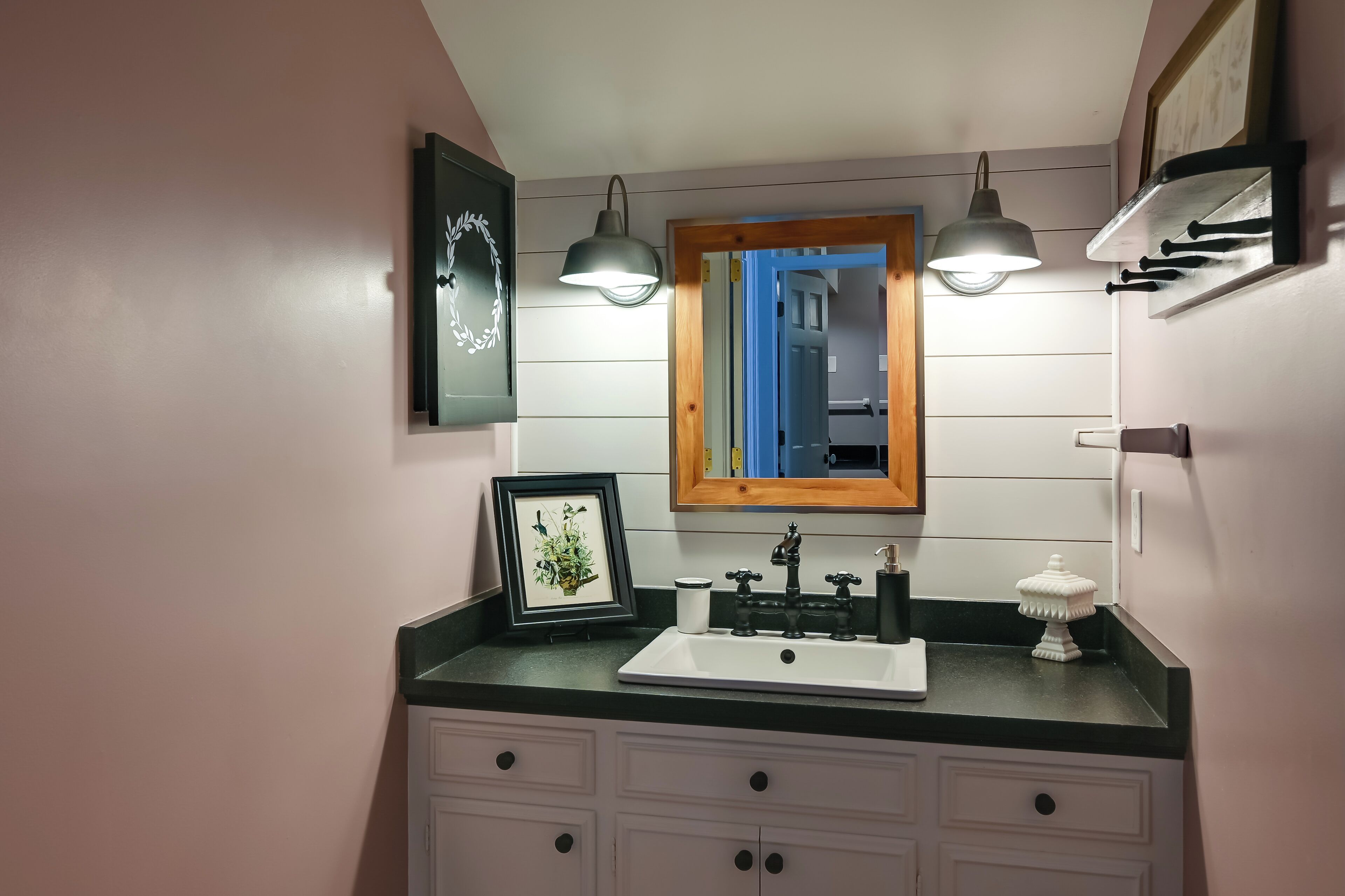 A bathroom with a white sink, black faucet, and two pendant lights. There are framed pictures on the wall and a small decorative item on the counter.