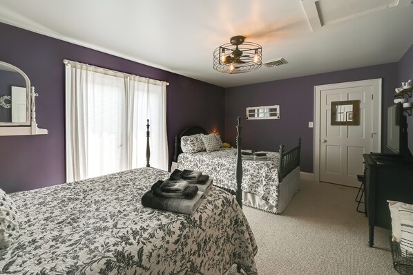 Une chambre avec deux lits, un ventilateur de plafond, une porte et une commode.