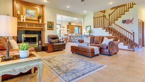 A spacious living room with a fireplace, leather sofas, a dining area, and a staircase with an American flag.