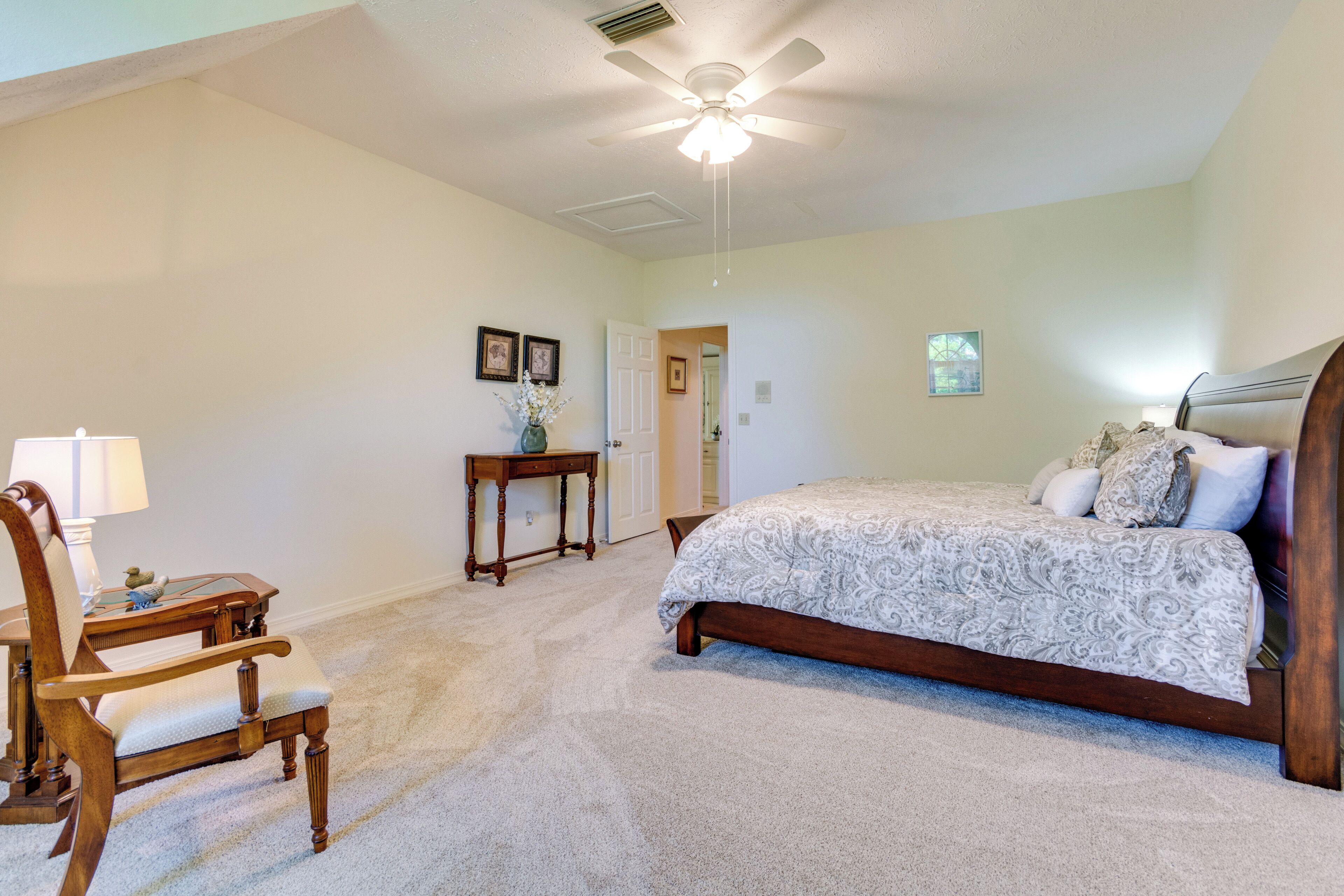 A bedroom with a bed, a chair, a table, and a ceiling fan.