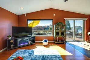 A living room with a flat-screen TV, a large window with an umbrella, and a view of the outdoors. - Waterfront Birch Bay Rental - Walk to Beach! (Blaine)