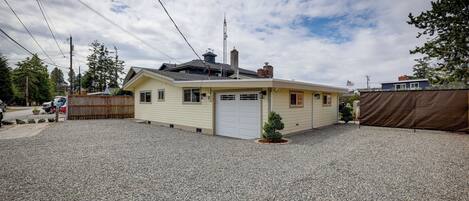Une maison de plain-pied avec un garage, un petit jardin devant et une allée en gravier.