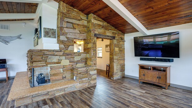 Un salon doté d’une cheminée en pierre, d’un plancher en bois, d’un téléviseur fixé au mur et d’un banc en bois.