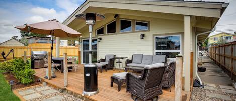 Un patio techado con mobiliario exterior, una parrilla y una pérgola con una lámpara.