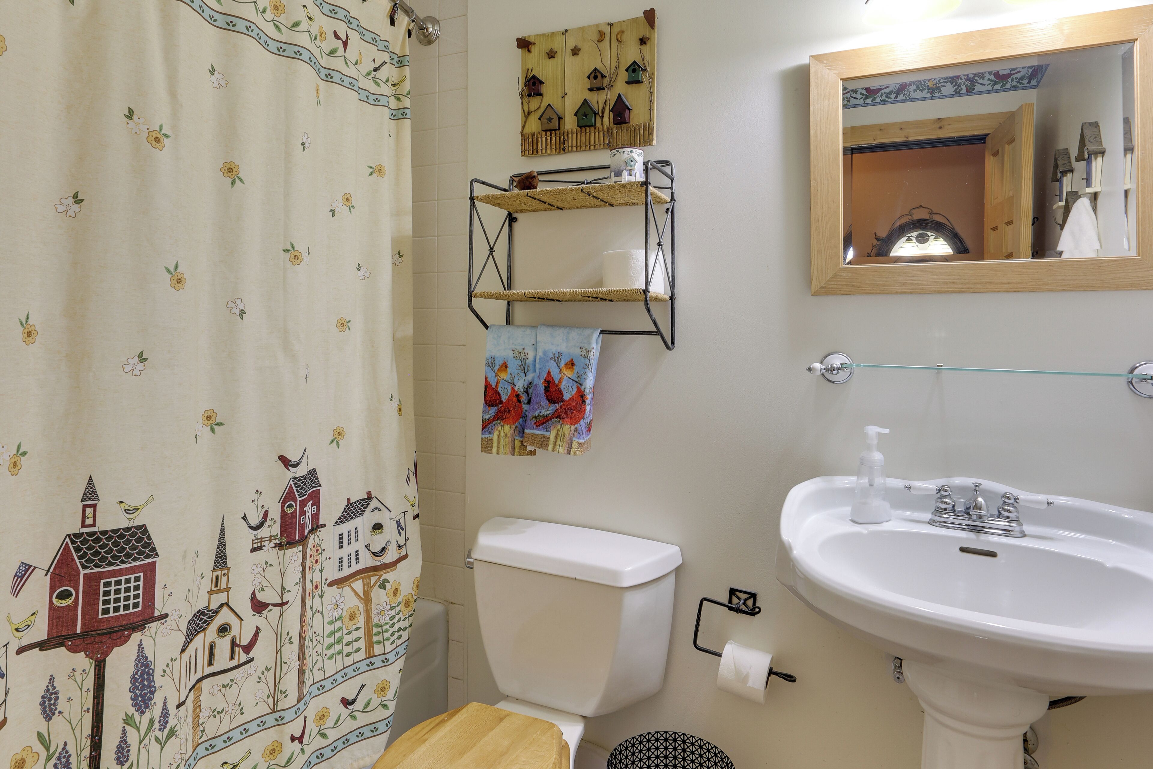 Et badeværelse med toilet, vask, spejl og et bruseforhæng med blomstermønster.